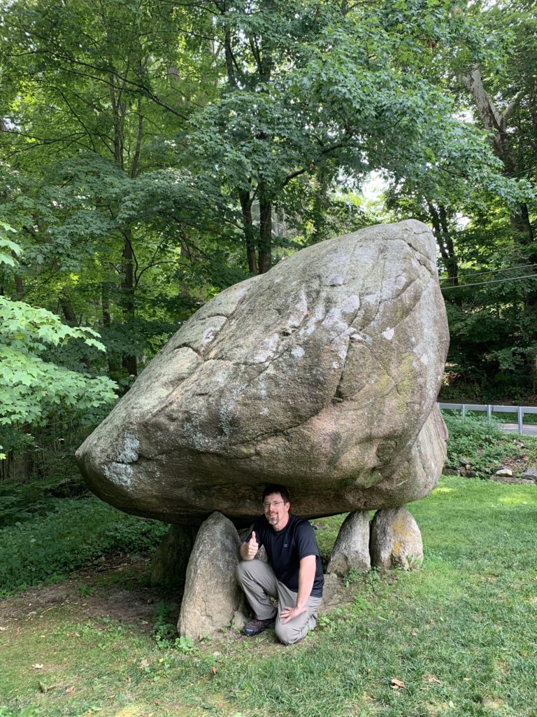 Wade Boman kneeling in front of Balanced Rock, North Salem, NY